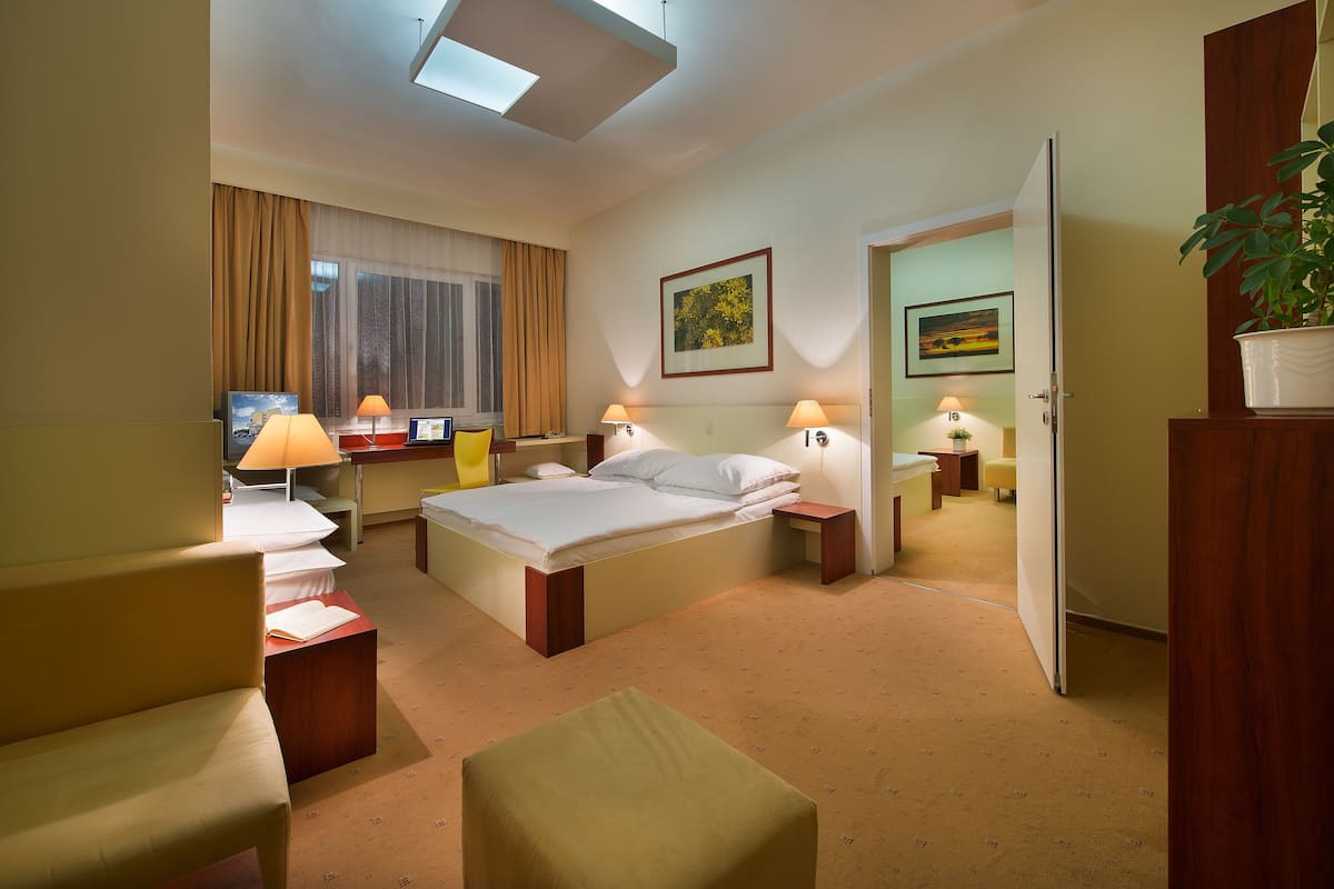 Een hotelkamer met een bed, twee nachtkastjes met lampen, een bureau met een stoel, een bank en een bijzettafeltje met een plant.