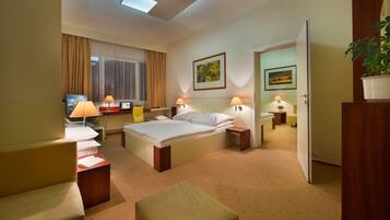 Een hotelkamer met een bed, twee nachtkastjes met lampen, een bureau met een stoel, een bank en een bijzettafeltje met een plant.