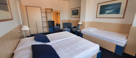 Quarto de hotel com cama, escrivaninha, cadeira, televisão, guarda-roupa e um quadro na parede.