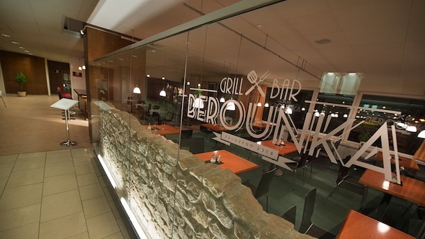 Un restaurante con pared de piedra y ventanas de vidrio, con un letrero que dice 'GRILL BAR BEROUNIA'.