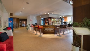 Vestíbulo de hotel con zona de bar, asientos rojos y un anuncio de Pepsi.