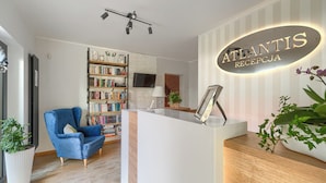 A reception area with a reception desk, a blue armchair, a bookshelf, and a sign that reads "Atlantis RECEPTIONJA". - Villa Atlantis (Kolobrzeg)