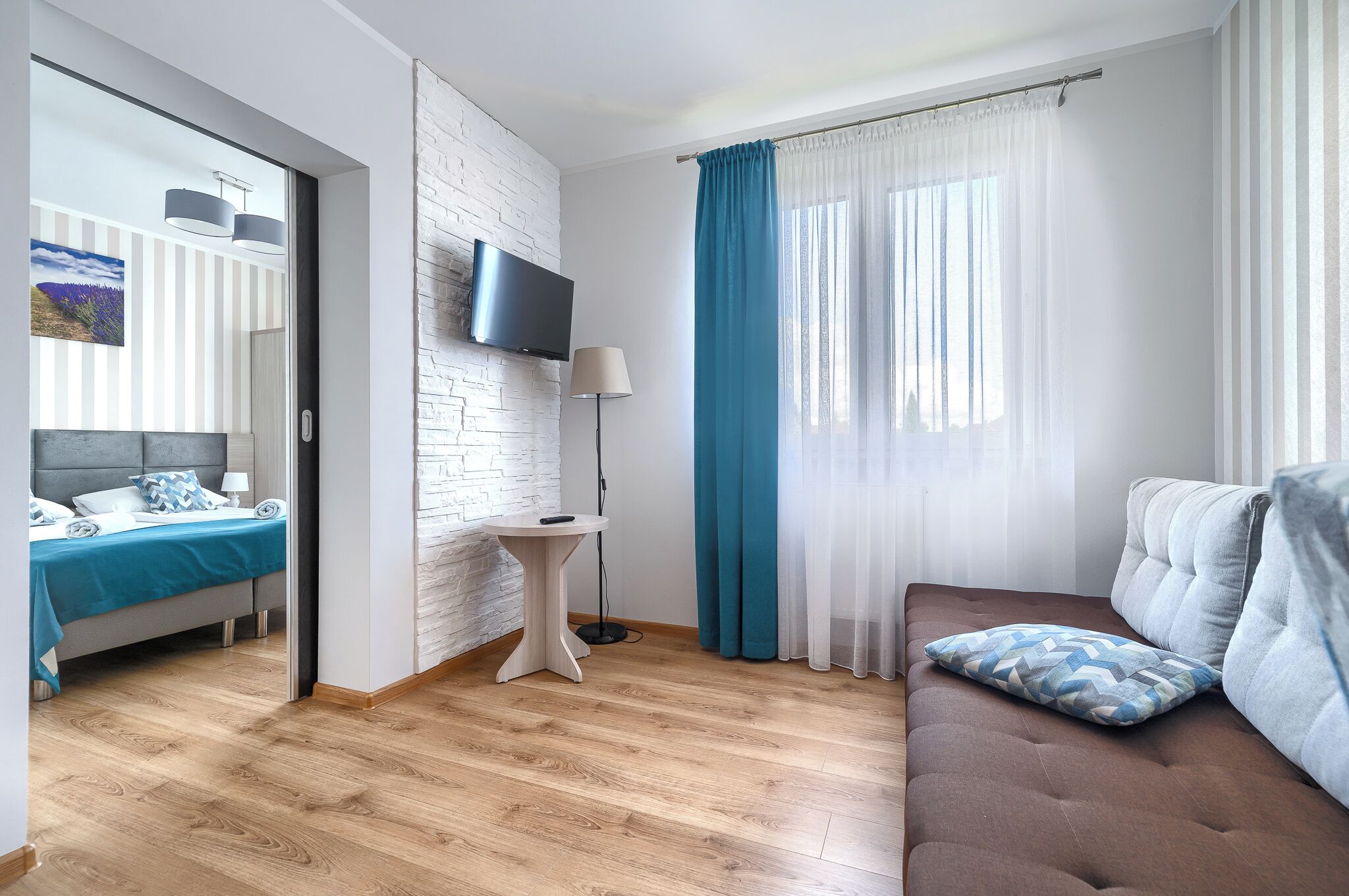 A modern hotel room with a bed, a sofa, a small table, and a TV.