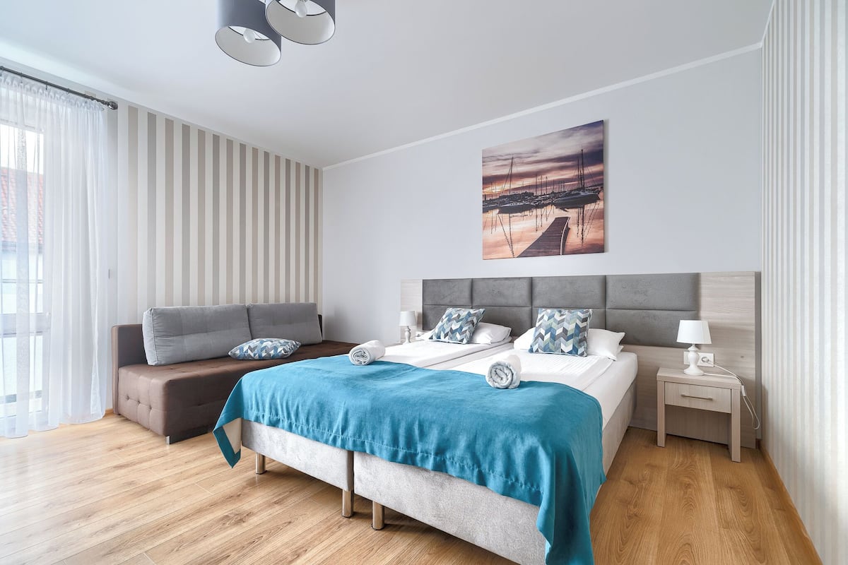 Un dormitorio moderno con una cama, mesitas de noche, un sofá y un cuadro en la pared.