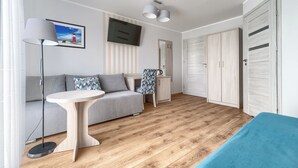 A modern room with a grey sofa, a round wooden table, a floor lamp, a TV, and a wardrobe. - Villa Atlantis (Kolobrzeg)