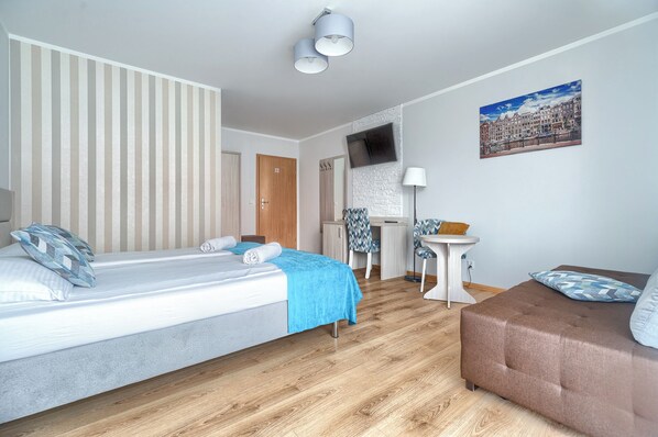 A hotel room with a bed, a sofa, a desk, and a TV on the wall. - Villa Atlantis (Kolobrzeg)