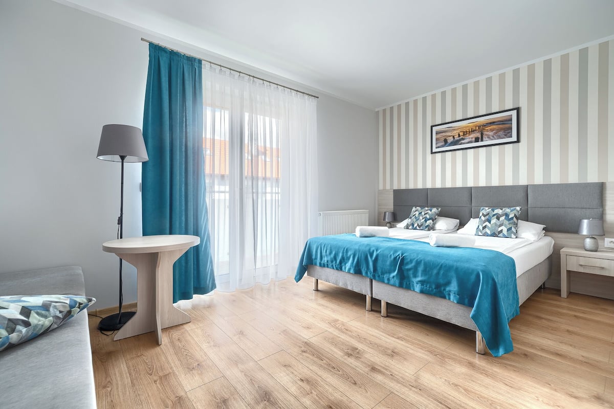 Un dormitorio moderno con cama, mesitas de noche, lámpara y vistas al exterior a través de amplios ventanales.