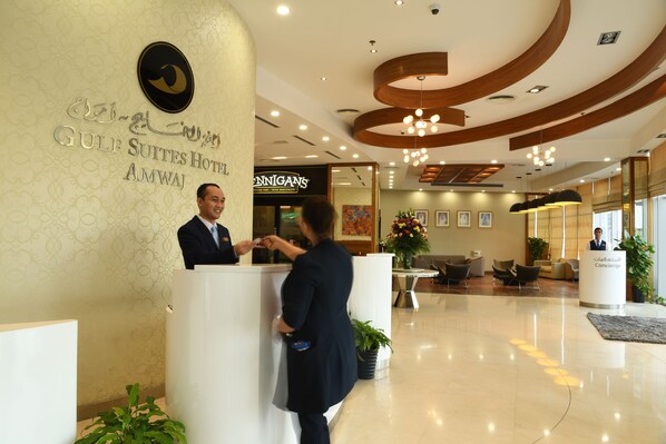 A hotel reception area with a modern design, including a reception desk, a concierge desk, and a seating area with chairs and a sofa.