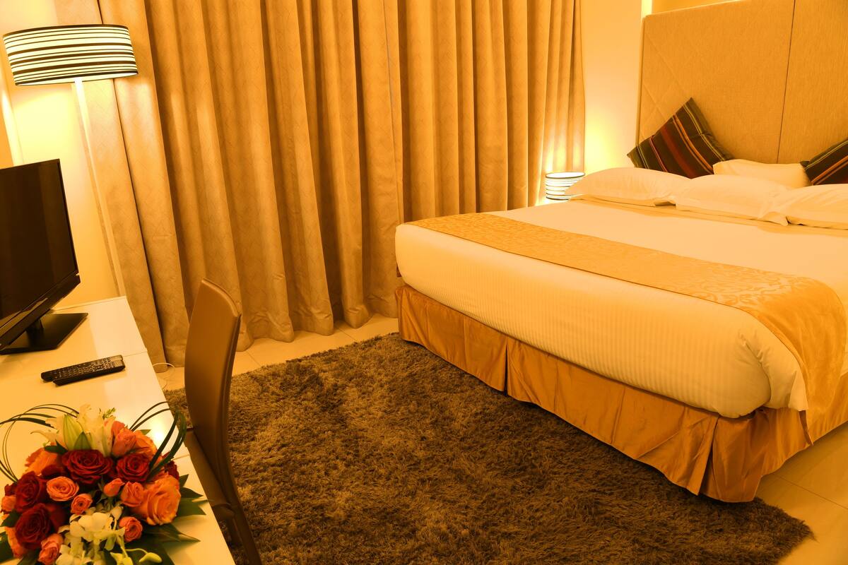 A hotel room with a bed, curtains, a remote control, a TV, and a floral arrangement.