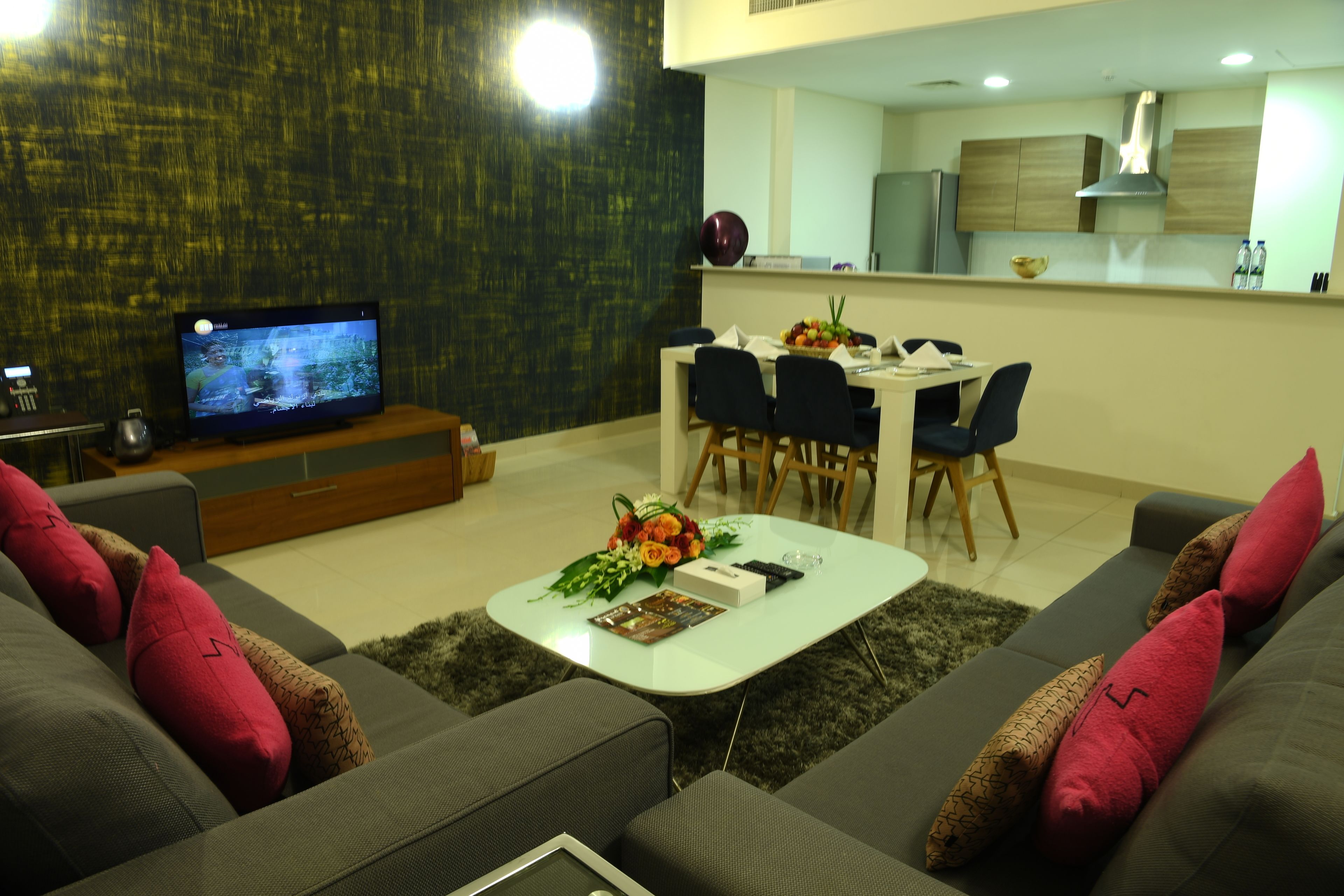 A modern living room with a sofa, coffee table, and a TV. There is a dining area with chairs and a table.