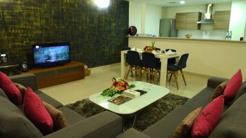 A modern living room with a sofa, coffee table, and a TV. There is a dining area with chairs and a table.