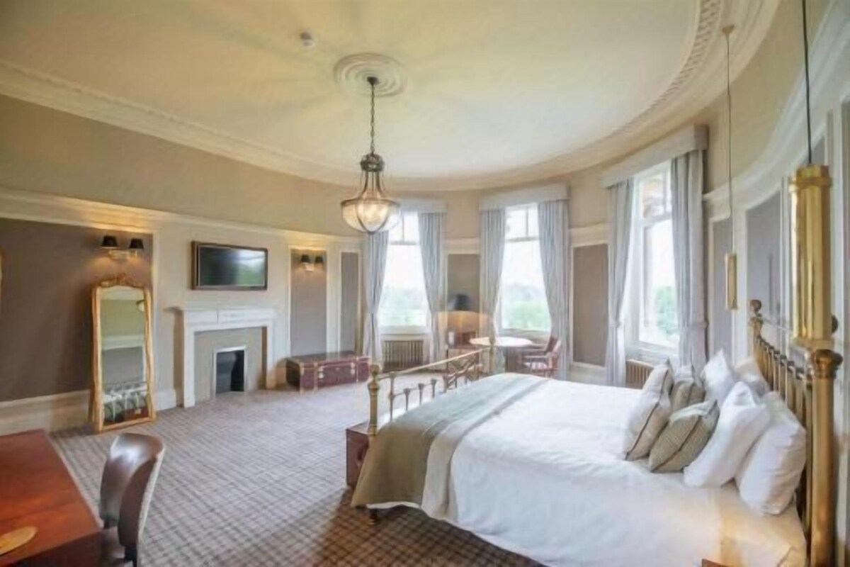Amplia habitación de hotel con una cama grande, un área de estar con chimenea y un televisor.