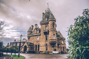 A historic stone building with a prominent tower, arched windows, and a well-maintained lawn. - Cornhill Castle Hotel (Biggar)