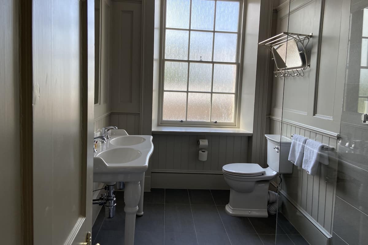 A bathroom with a window, two sinks, a toilet, and a towel rack.