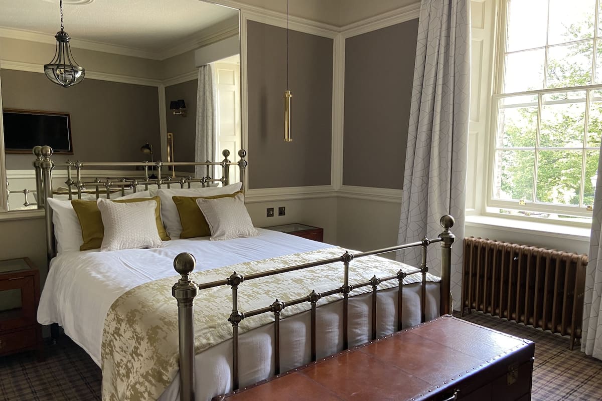 A neatly arranged bedroom with a large bed, a wooden bench, a radiator, and a window with curtains.