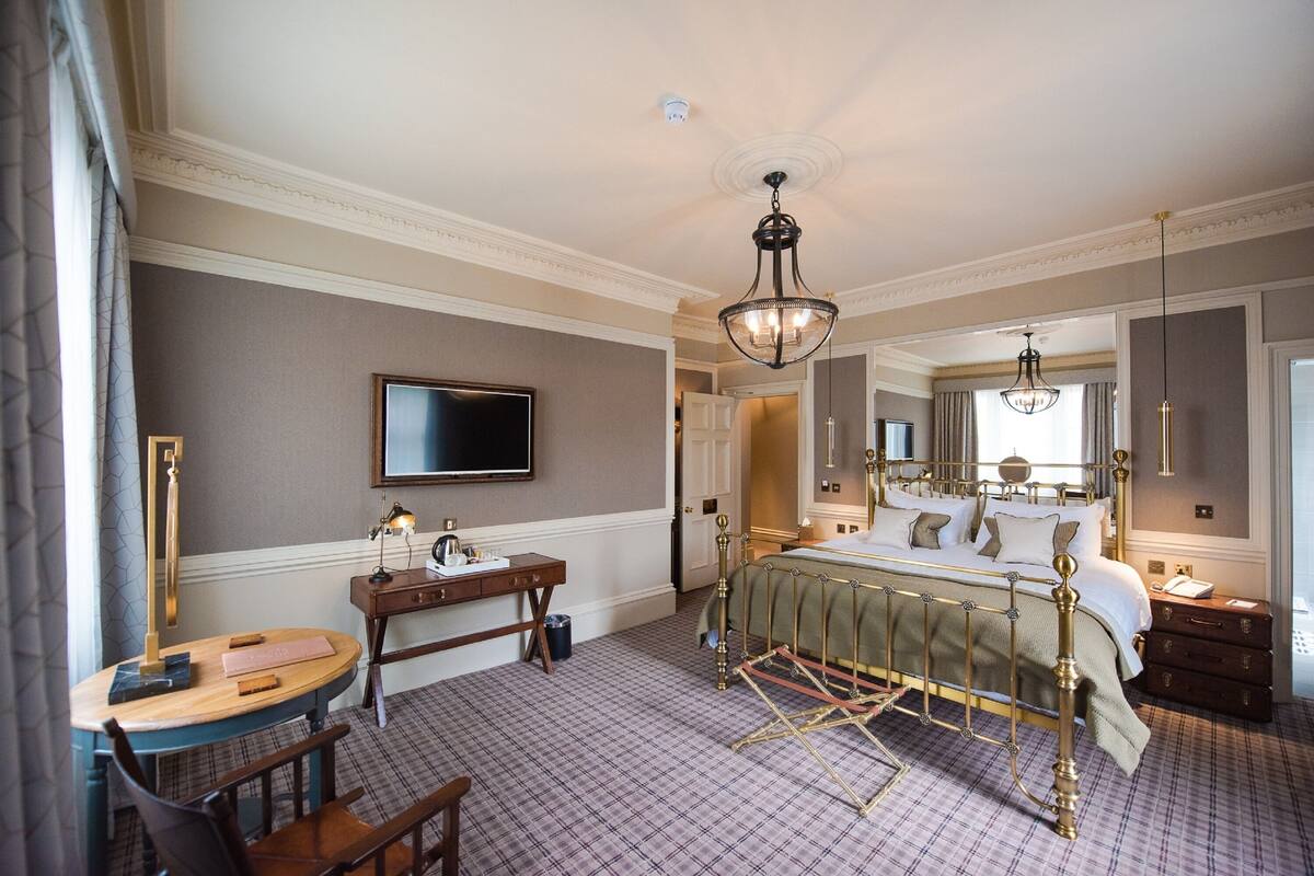 A hotel room with a large bed, a desk with a chair, a television, and a chandelier.