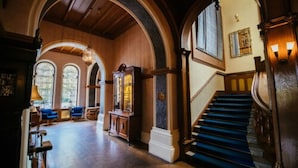 Un salón imponente con altos techos de madera, amplias ventanas arqueadas y una escalera con alfombra azul.