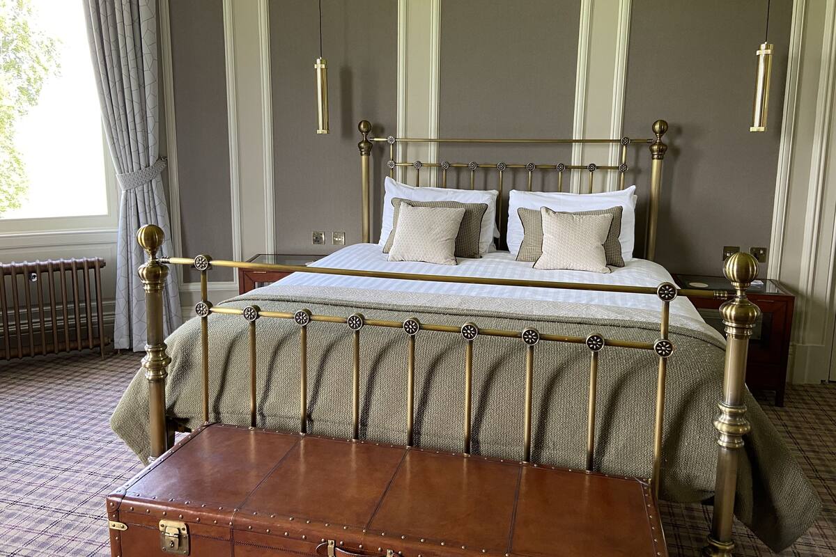 A classic four-poster bed with a brass frame, a wooden bench, and a radiator on the floor.