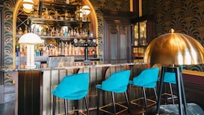 Una zona de bar con mostrador, taburetes azules y una lámpara decorativa.