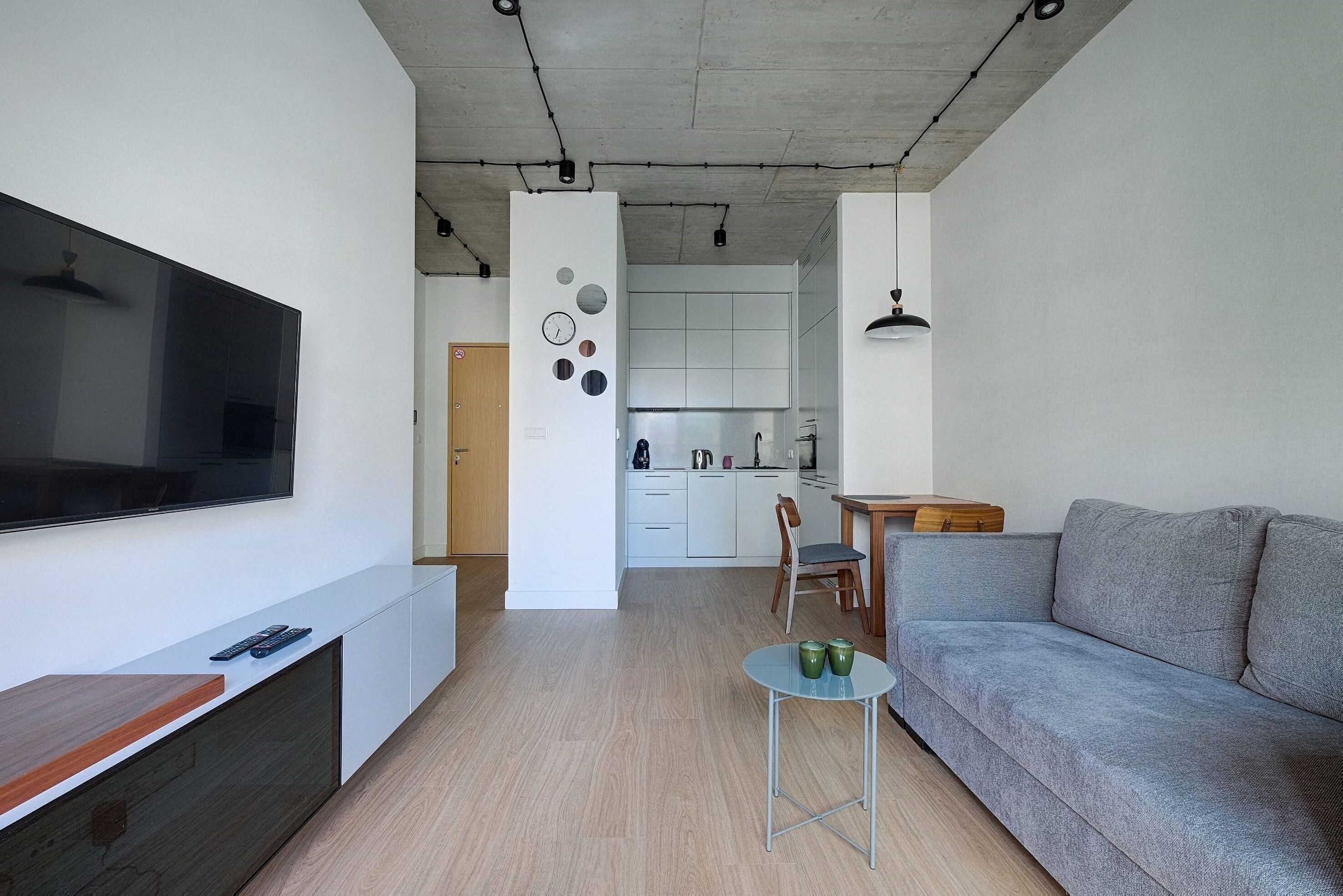 A modern living room with a flat-screen TV, a grey sofa, and a small table with green cups.