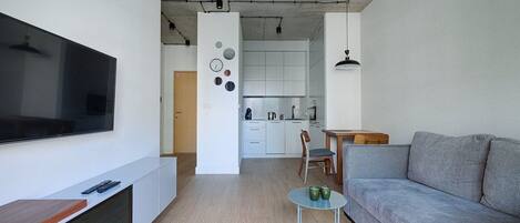 A modern living room with a flat-screen TV, a grey sofa, and a small table with green cups.
