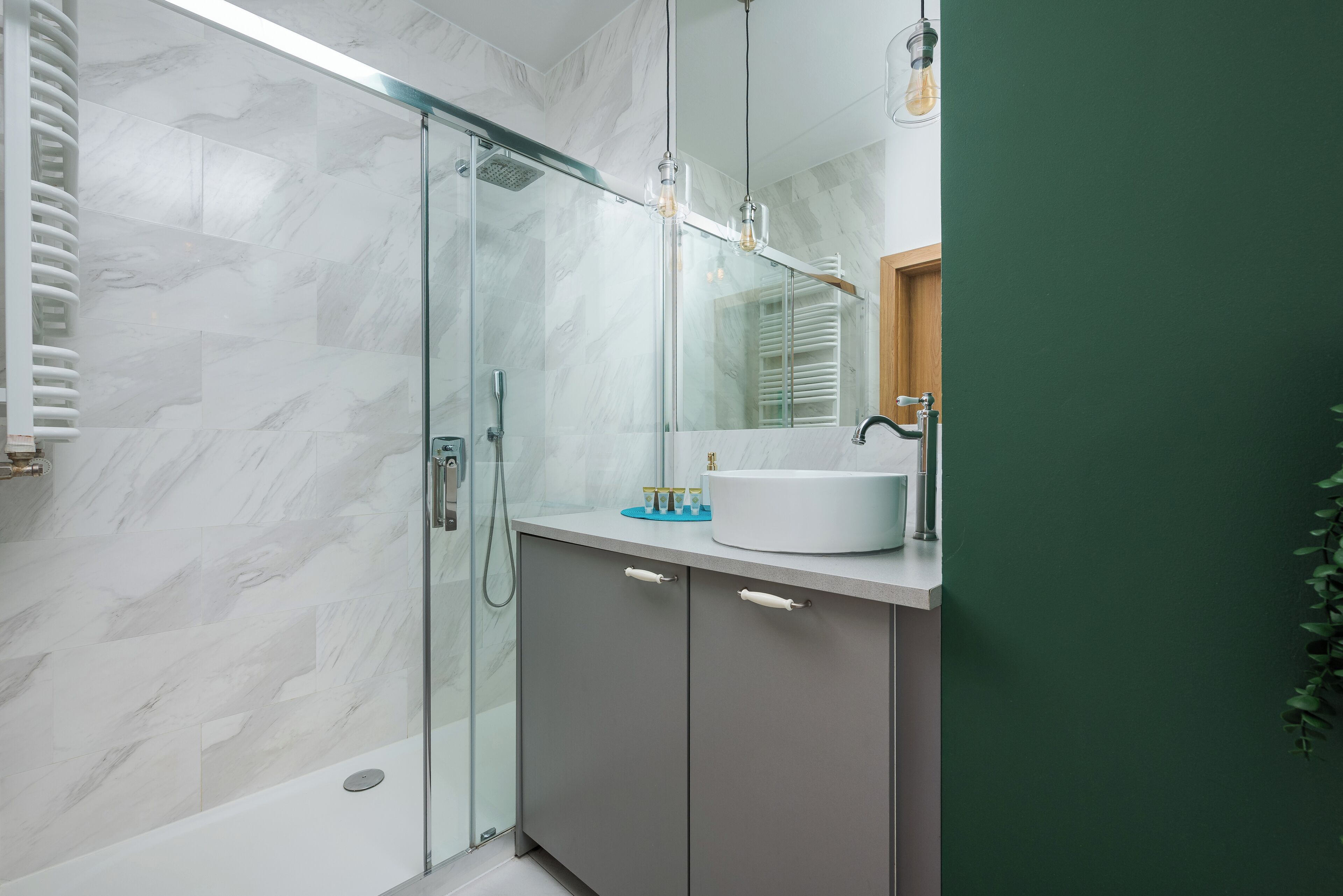 Een moderne badkamer met een douchecabine van glas, een wit wastafelmeubel en een groene accentmuur.
