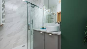Een moderne badkamer met een douchecabine van glas, een wit wastafelmeubel en een groene accentmuur.
