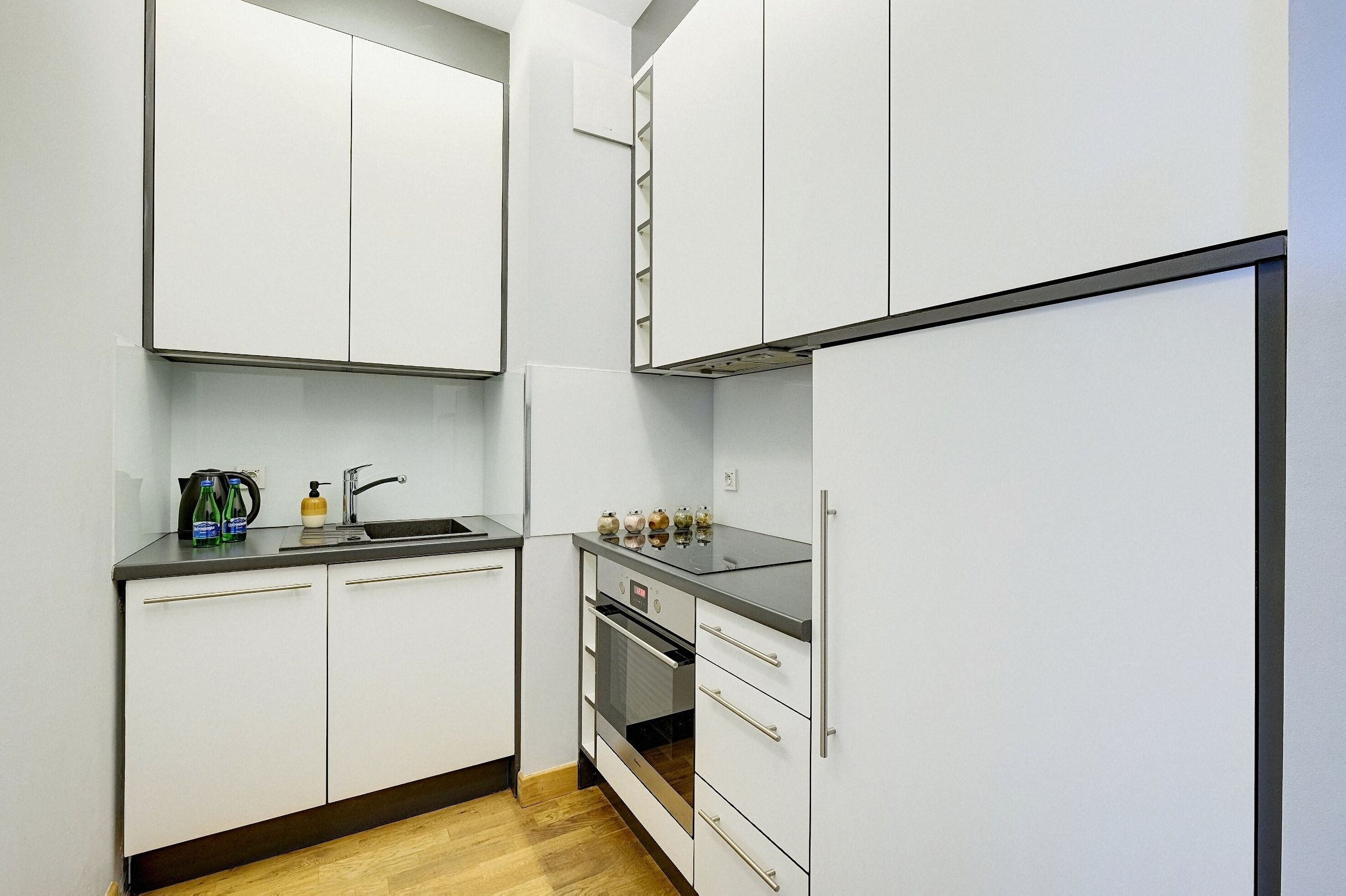 A compact kitchen with white cabinets, a black countertop, and a built-in oven.