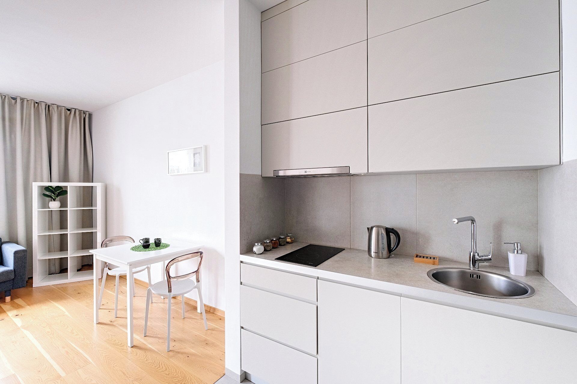 A modern kitchen with white cabinetry, a stainless steel sink, and a black induction cooktop.