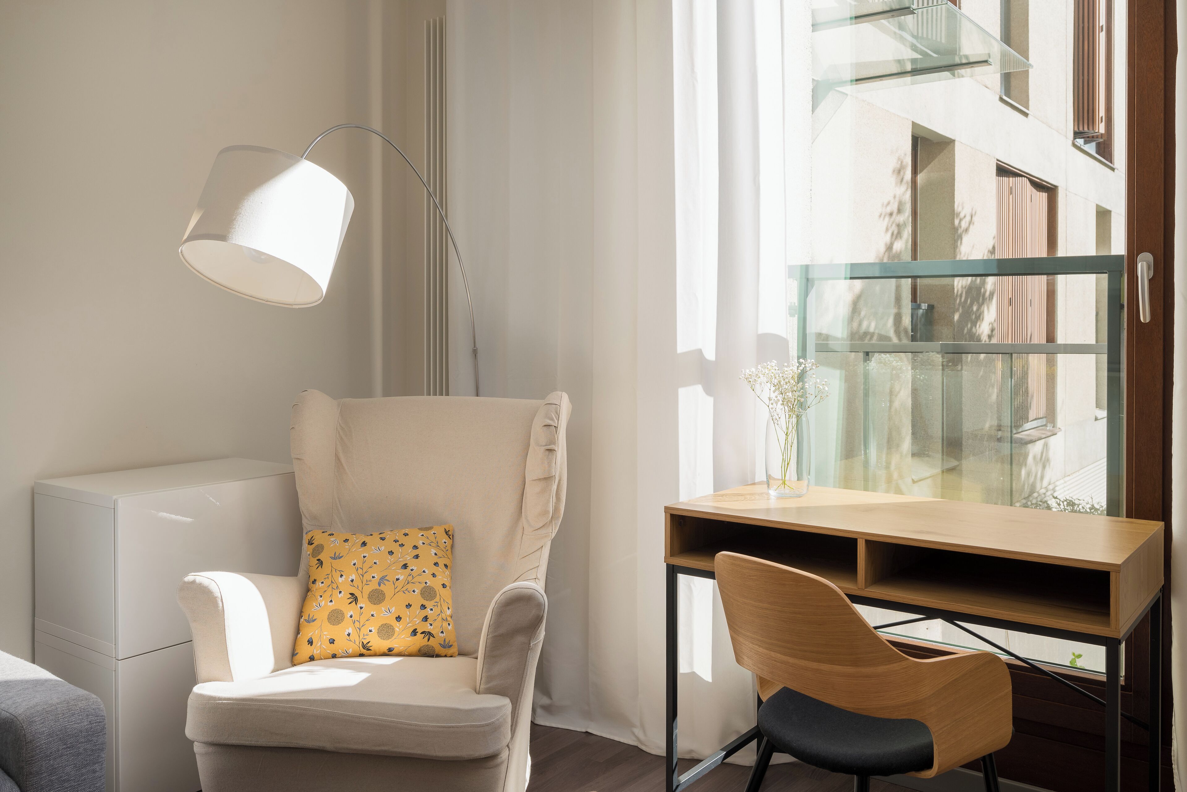 A modern room with a white armchair, a wooden desk, and a floor lamp.