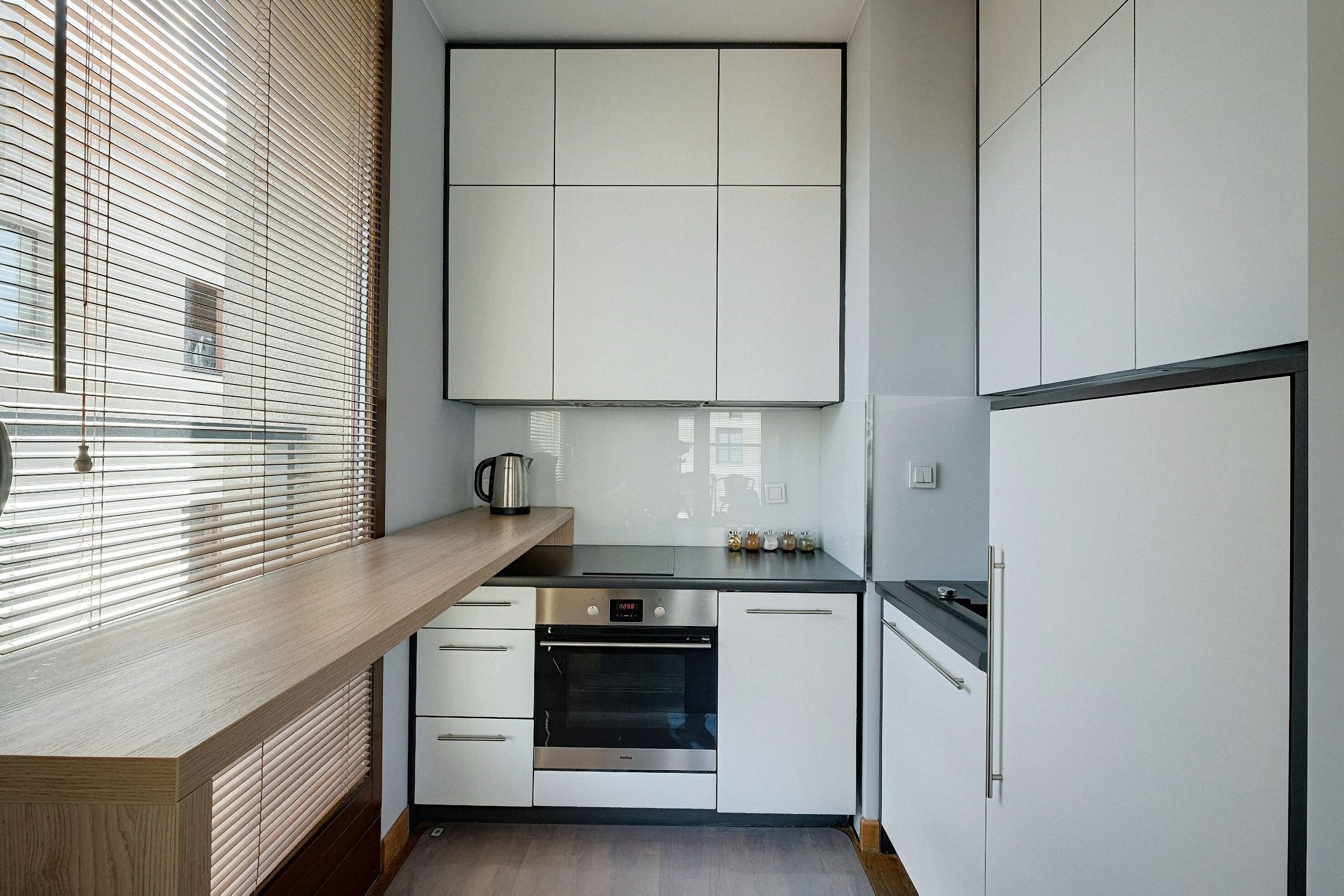 A modern kitchen with white cabinets, a wooden countertop, a built-in oven, and a refrigerator.