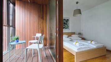 A modern bedroom with a wooden bed, a small table with chairs, and a view through a sliding door.