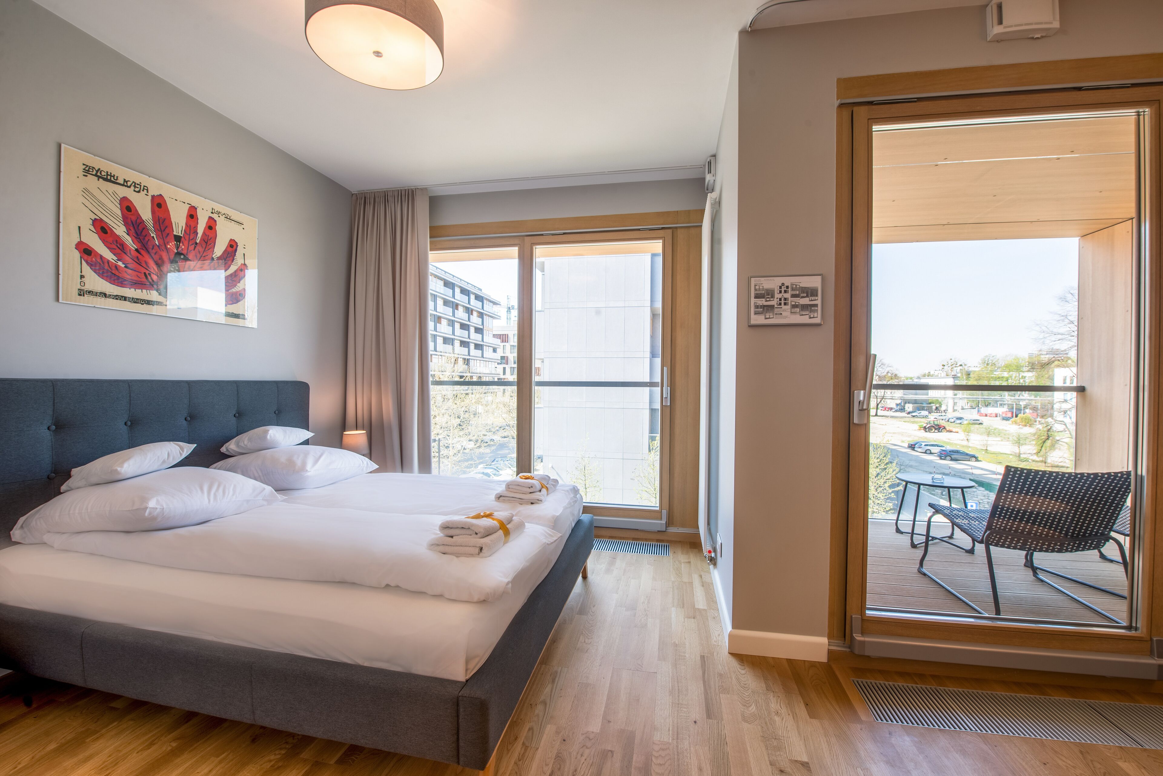 Habitación de hotel con una cama grande, vistas al exterior y un balcón con mesa y silla.