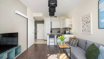 A modern living room with a flat-screen TV, a sofa, a coffee table, and a dining area with a kitchen in the background.