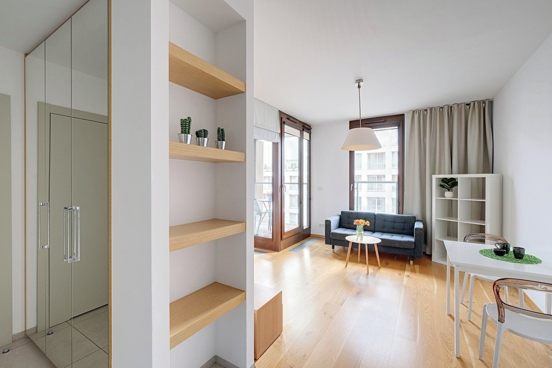 A modern living room with a sofa, a dining table, and a coffee table. There are wooden shelves and a white cabinet.