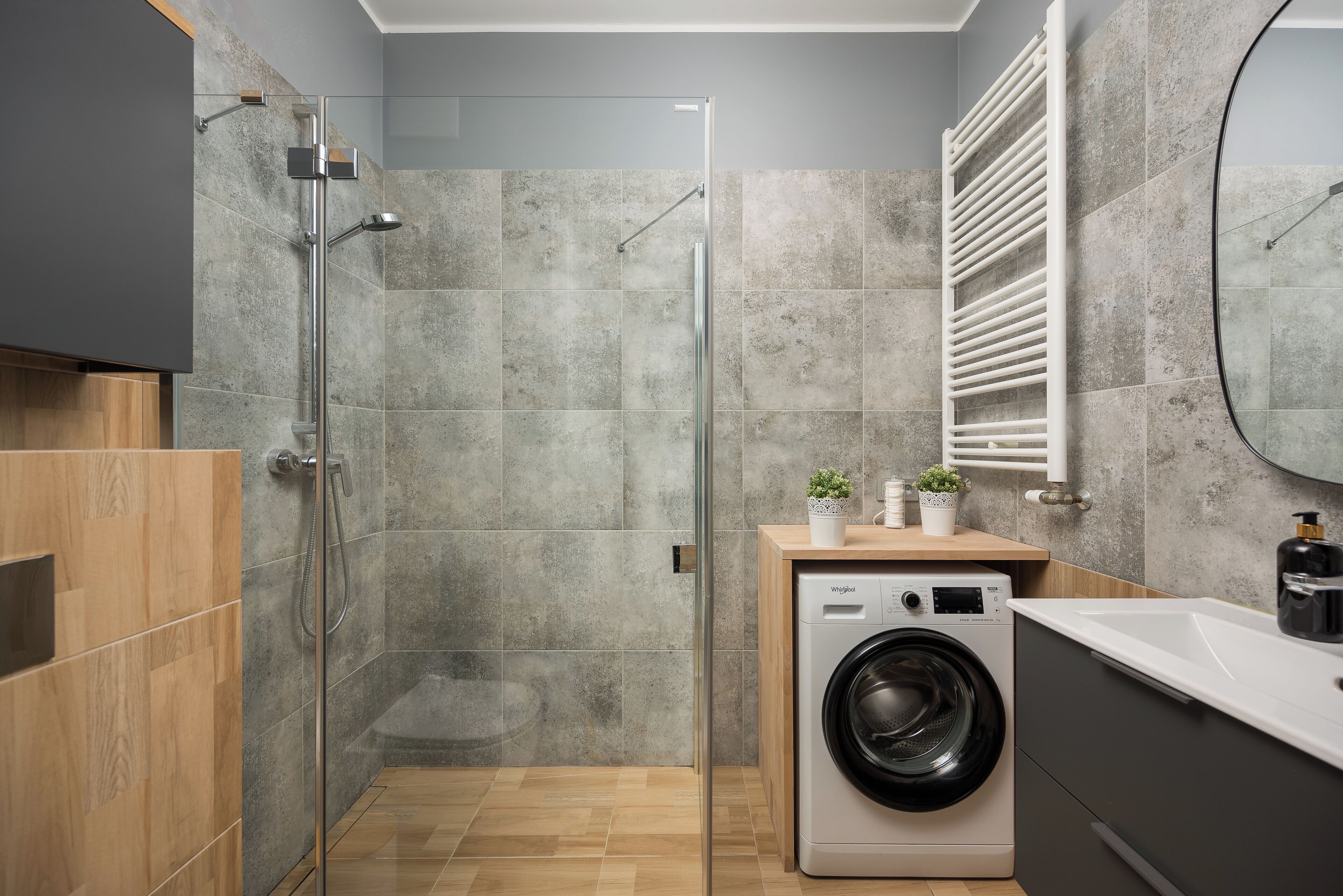 A modern bathroom with a glass shower enclosure, a built-in washing machine, and a wooden vanity.