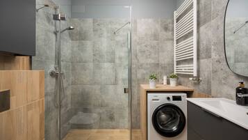 A modern bathroom with a glass shower enclosure, a built-in washing machine, and a wooden vanity.