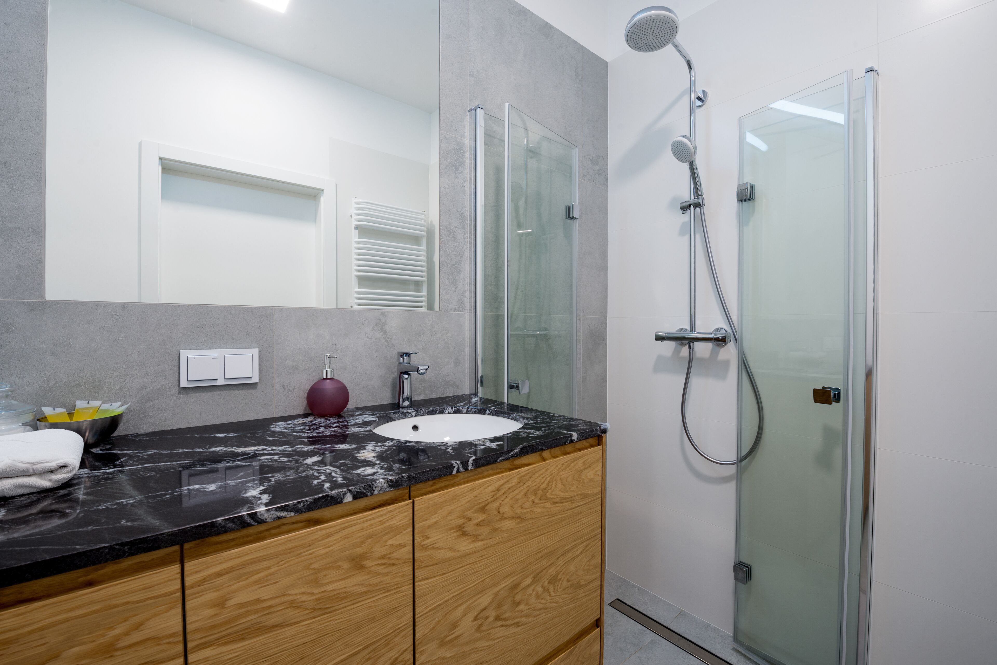 A modern bathroom with a marble countertop, wooden cabinets, a glass shower enclosure, and a white sink.