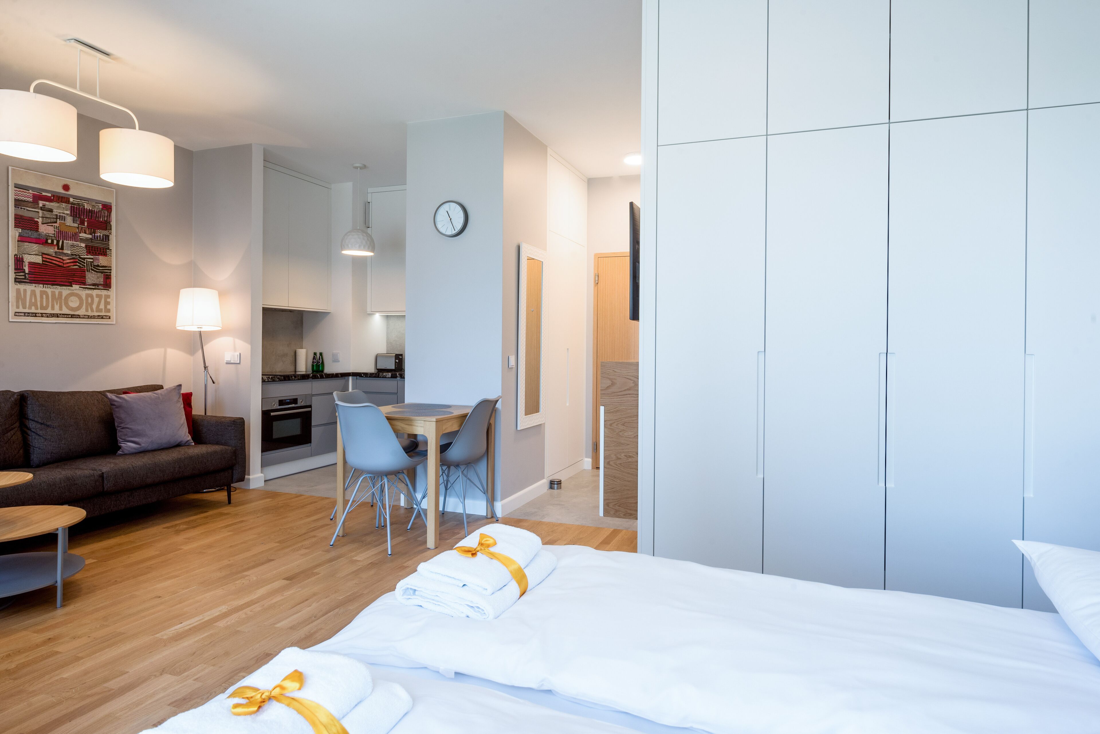 Una camera d'albergo moderna con un letto ben rifatto, un divano, una zona pranzo e una cucina sullo sfondo.