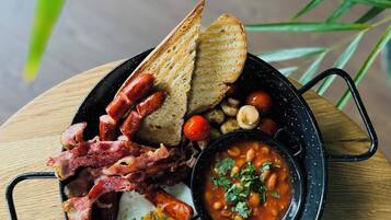 Une assiette de petit-déjeuner comprenant des toasts, du bacon, des œufs, des haricots et une portion de soupe.