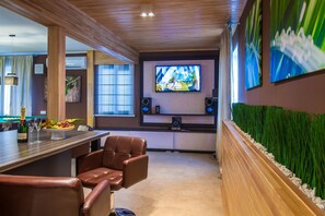 A modern bar area with leather chairs, a fruit bowl, and a television screen.