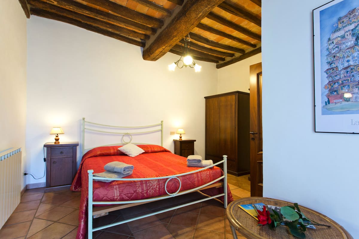 Een slaapkamer met een bed, nachtlampjes, een houten garderobe en een ingelijst schilderij aan de muur.