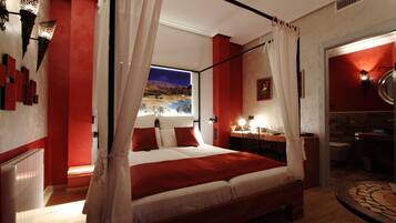 A bedroom with a large bed, red accents, a nightstand, and a view of a landscape through a window.