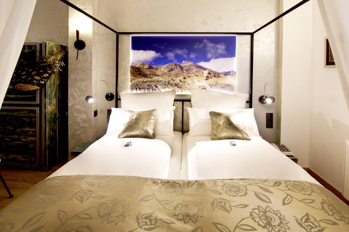 A room with a bed, a painting of a mountain landscape, and a mirror.