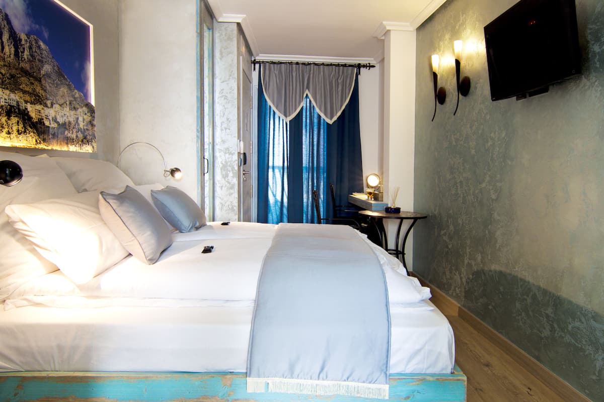 A neatly made bed with white linens, a bedside table with a lamp, and a wall-mounted TV.