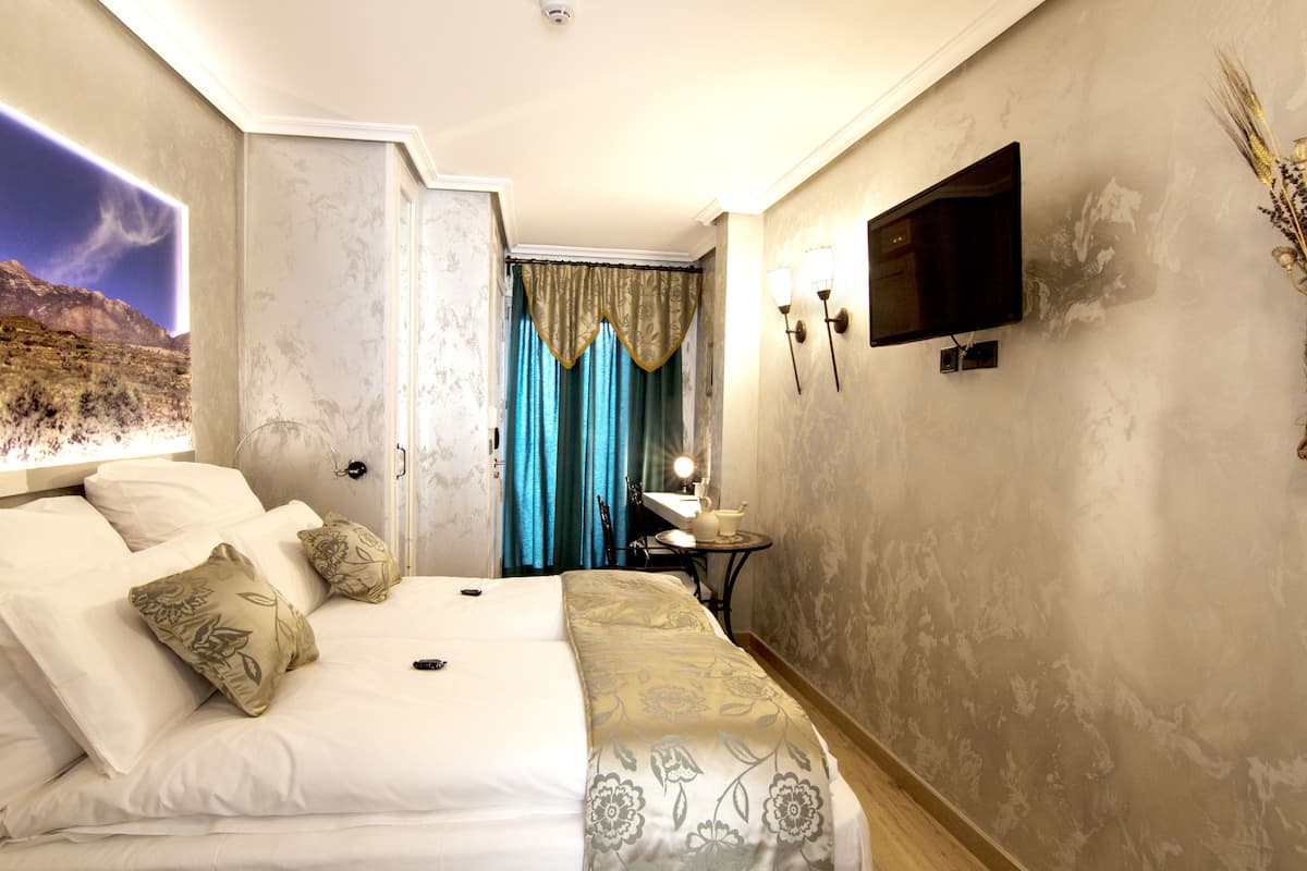 A hotel room with a bed, a television, a small table with a lamp, and a bathroom visible through a curtain.