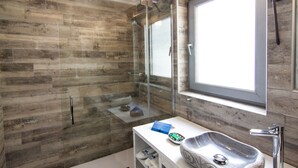 Een moderne badkamer met een stenen wastafel, een douchecabine van glas en een groot raam.