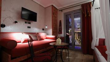 Una sala de estar acogedora con un sofá rojo, un televisor de pantalla plana montado en la pared y una pequeña mesa redonda con sillas.