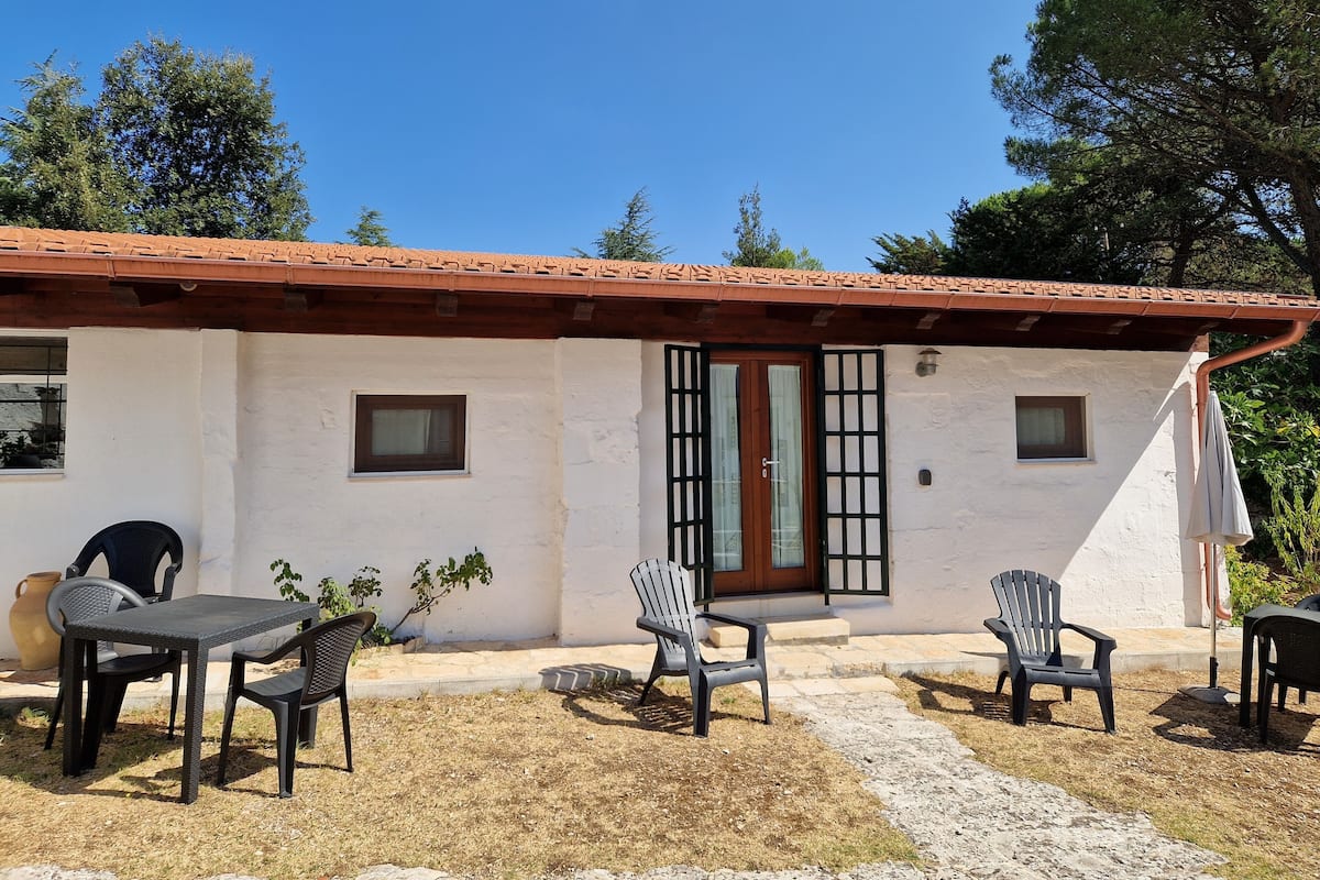A single-story building with a tiled roof, a front door with a window, and a small porch area with outdoor seating.