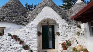 Una casa de piedra tradicional con fachada blanca, puerta verde y numerosos maceteros alrededor de la entrada.